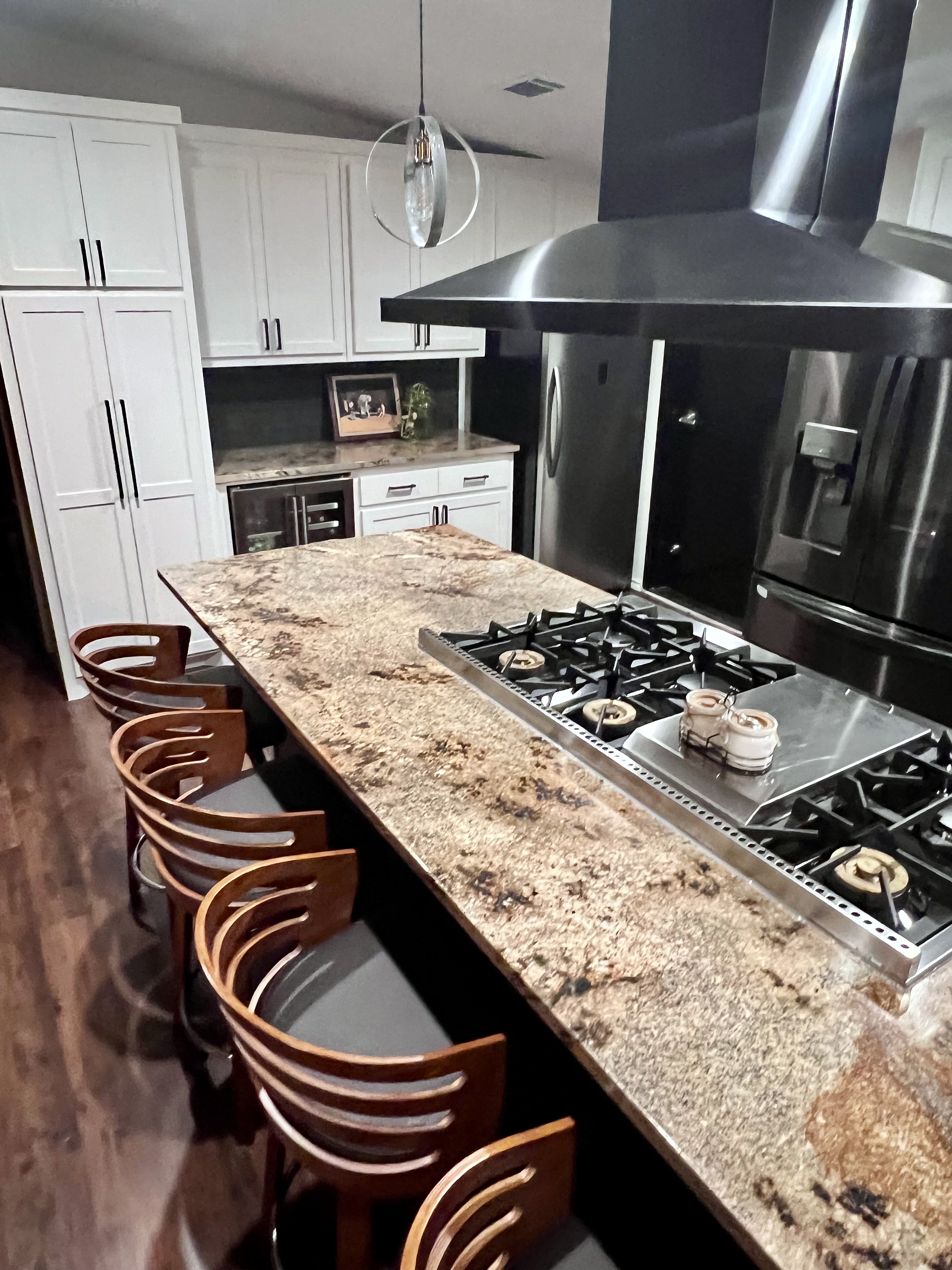 Buckhorn kitchen after — island end showing gas cooktop, bar stools with wood backs, granite surface and pendant light