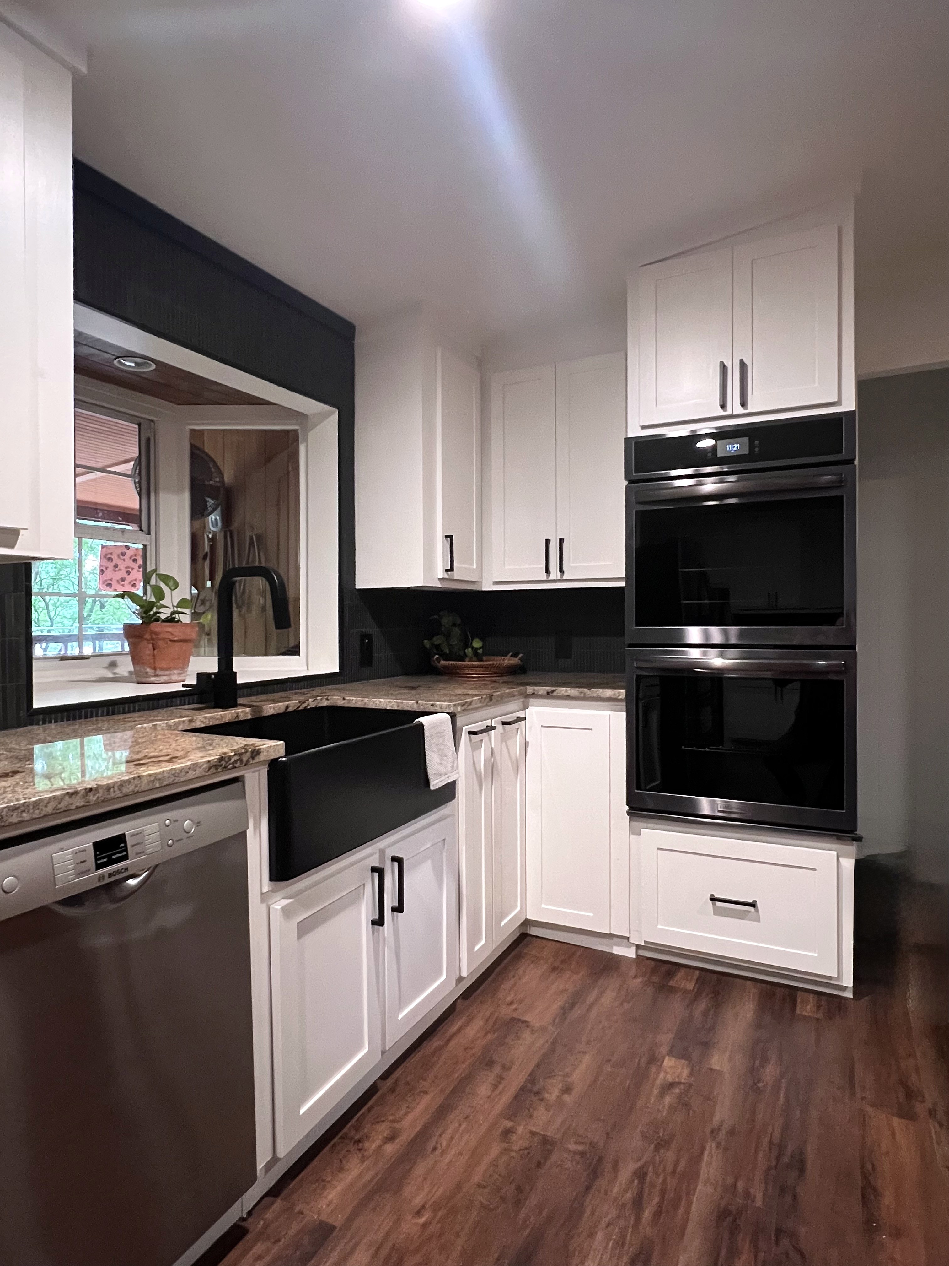 Buckhorn kitchen after — sink wall with black matte farmhouse sink, black gooseneck faucet, window above sink framed in matte black and white shaker cabinets