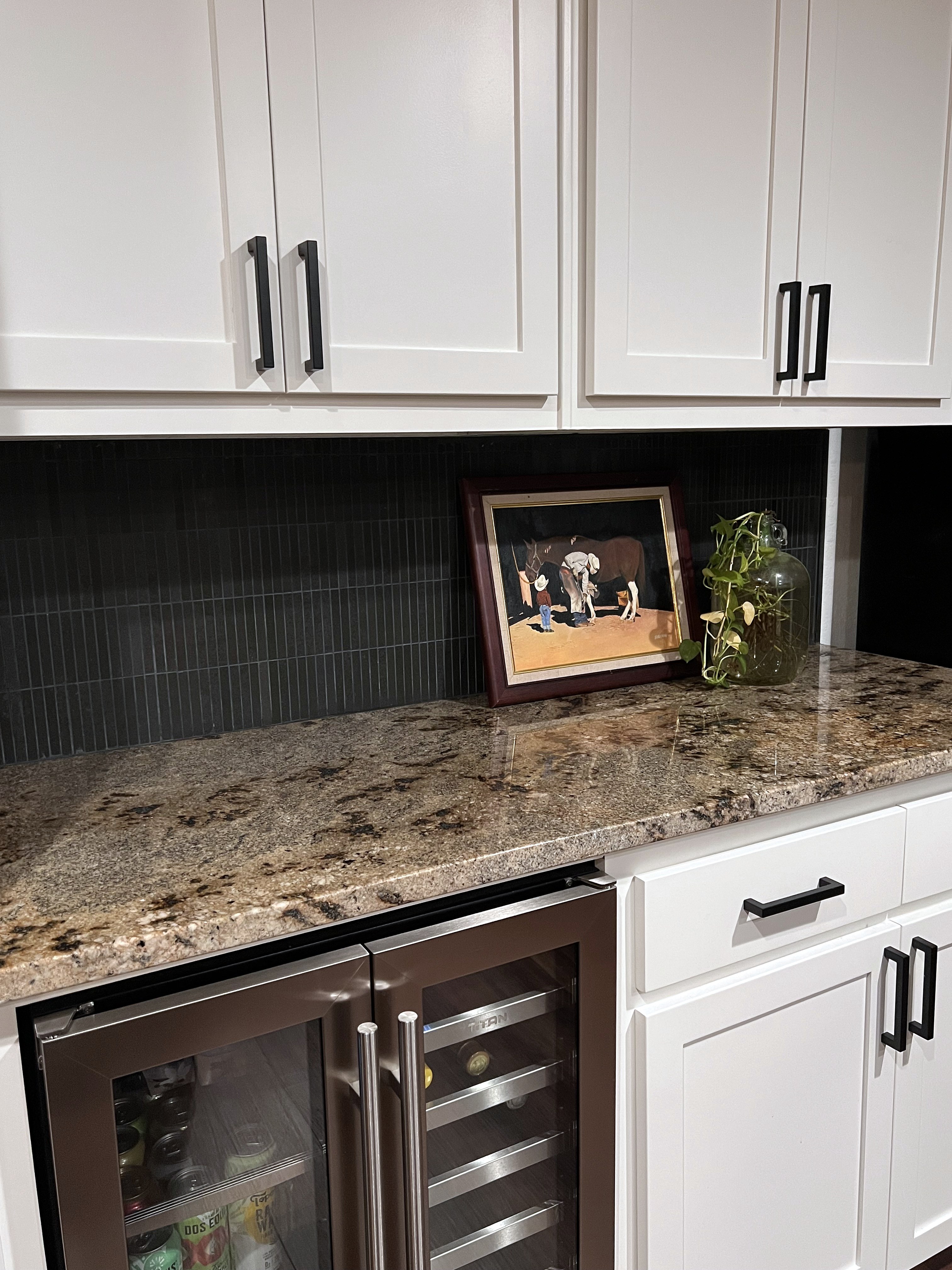 Buckhorn kitchen after — counter detail with black vertical tile backsplash, framed cowboy artwork and beverage cooler below