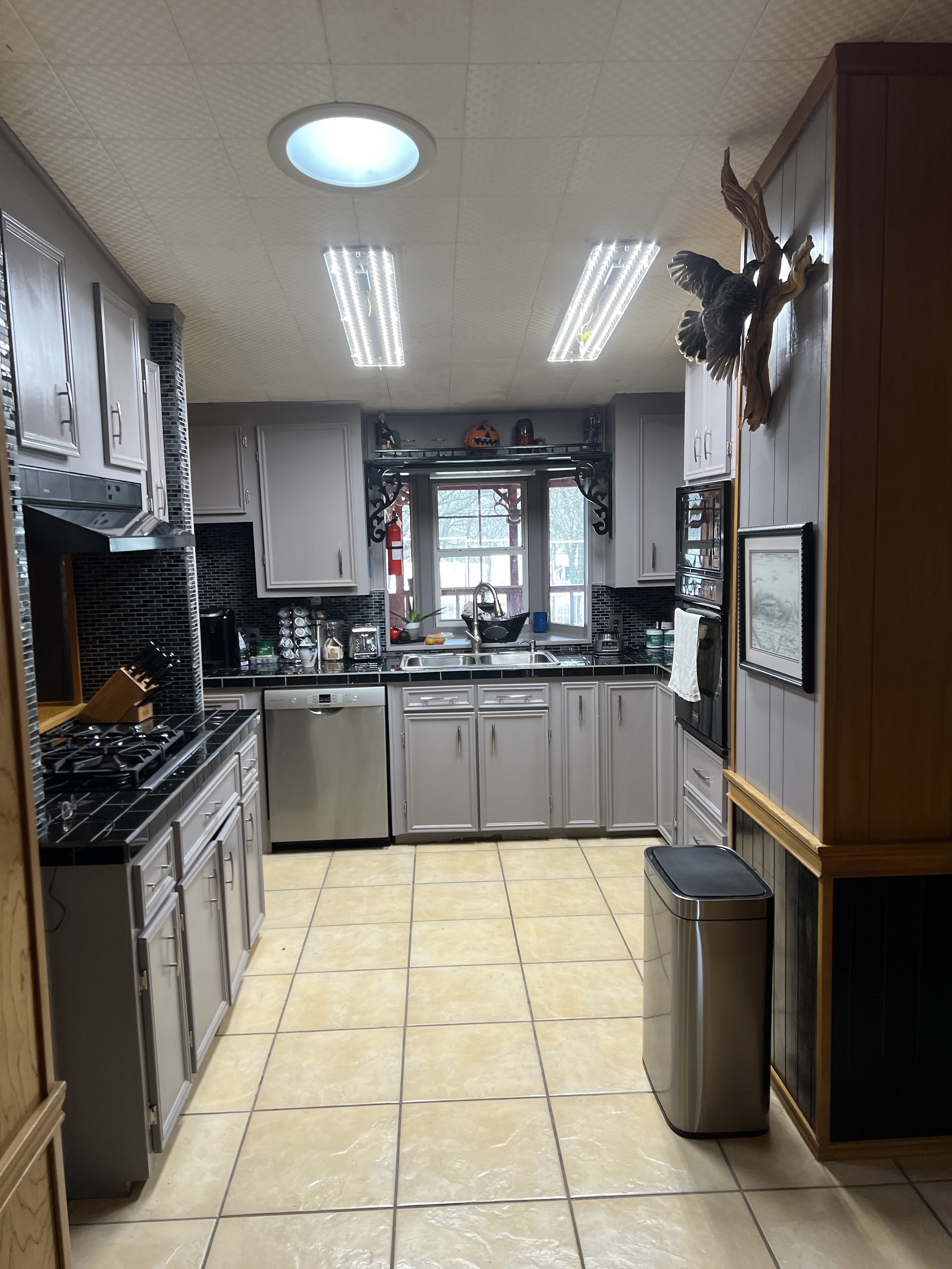 Buckhorn kitchen before — dated gray cabinets, black tile countertops, tile floor and original fluorescent lighting looking toward the sink wall