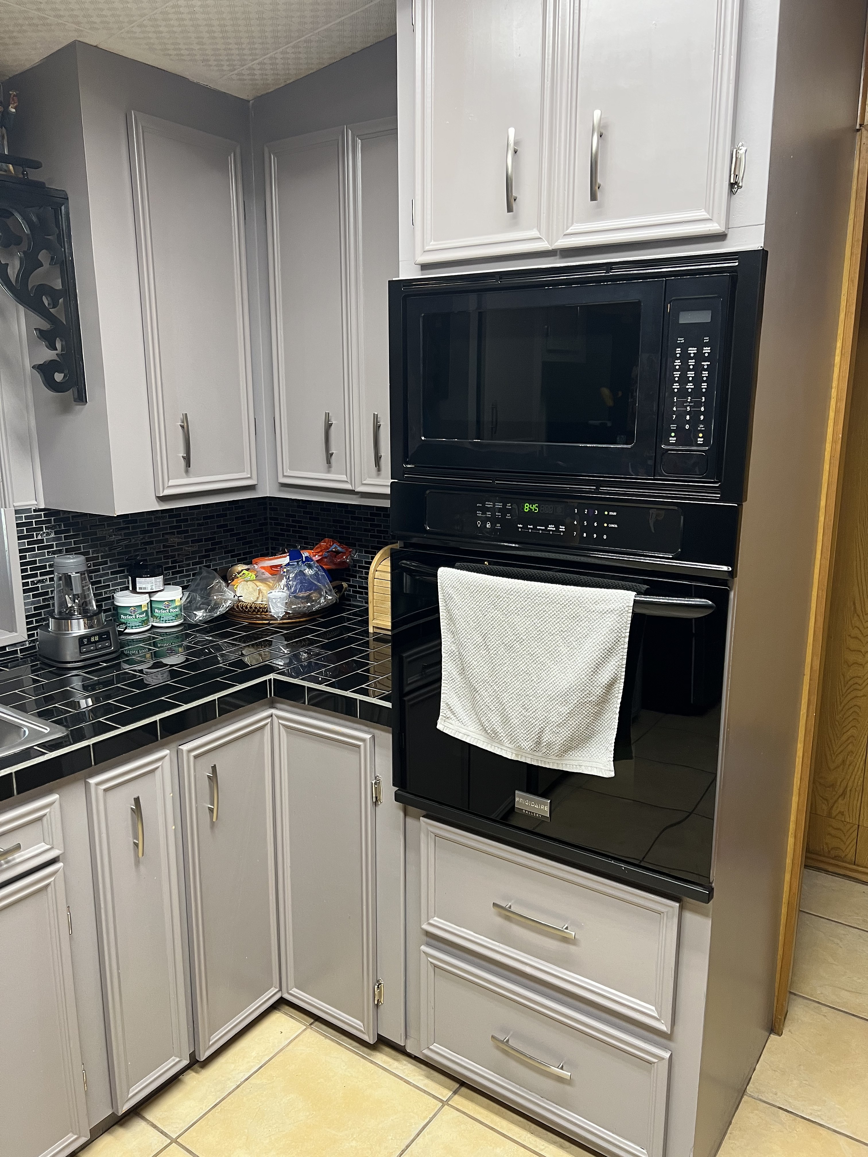 Buckhorn kitchen before — original wall oven and microwave in corner with gray cabinets and black tile countertop