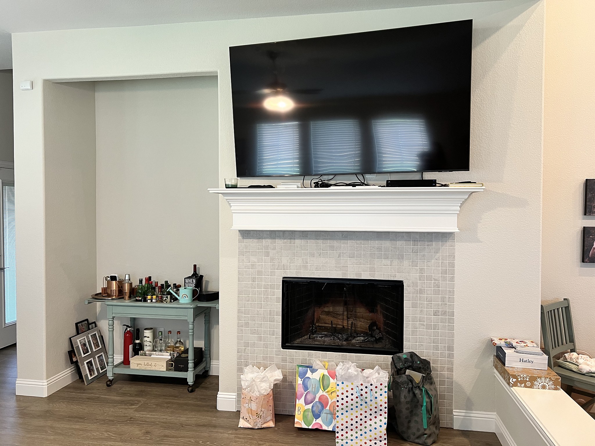 Half Moon before — original builder-basic fireplace with white tile surround, open recessed niche, exposed television cords and bar cart beside the hearth