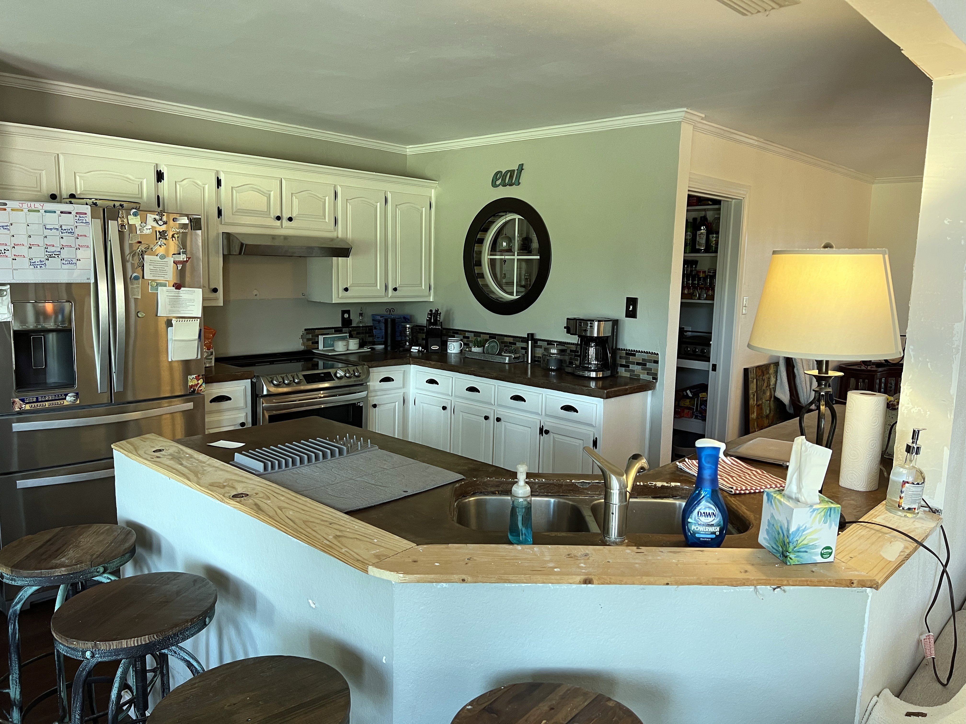 Millbrook kitchen before — original white arched cabinets, dark countertops, mosaic tile backsplash, round window and peninsula sink