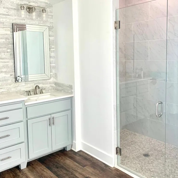 Old Gin bathroom — sage vanity, stone tile backsplash and glass shower enclosure