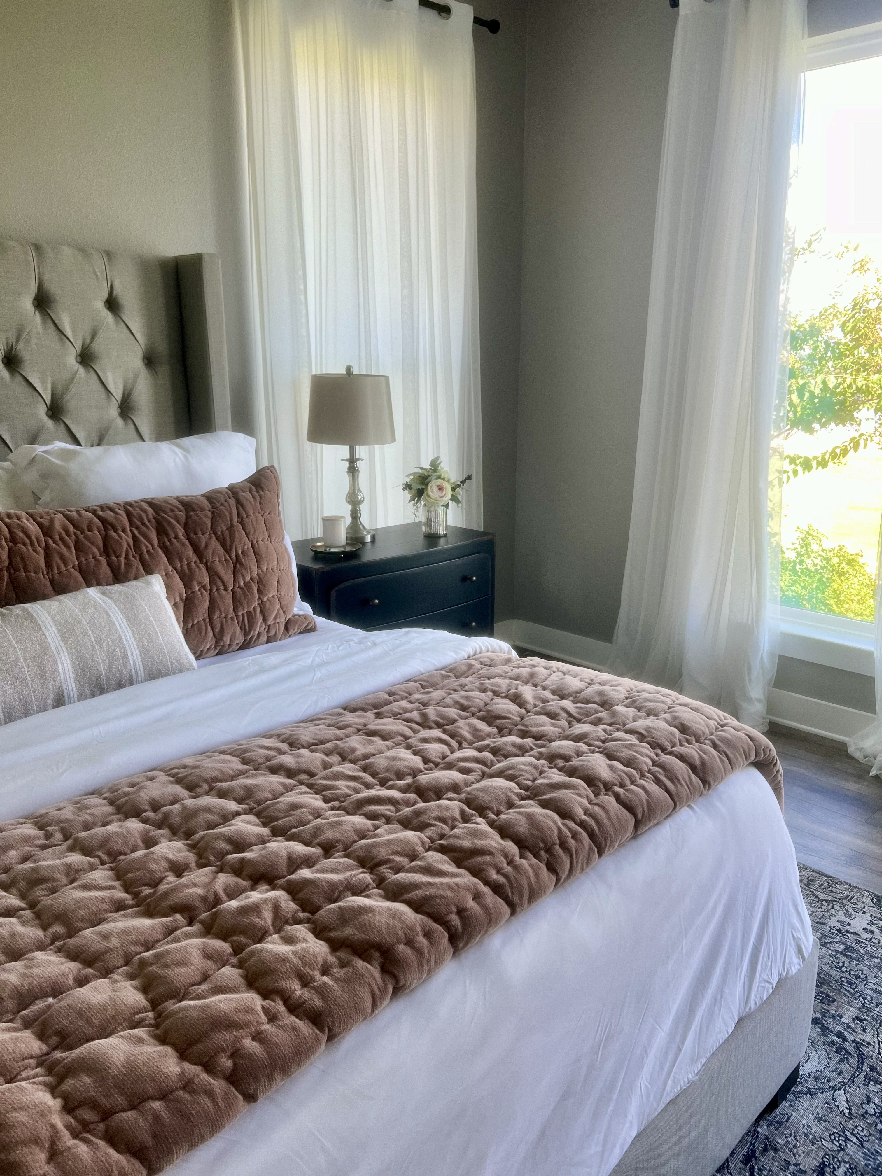 Old Gin bedroom — tufted headboard, mauve throw and nightstand with garden view
