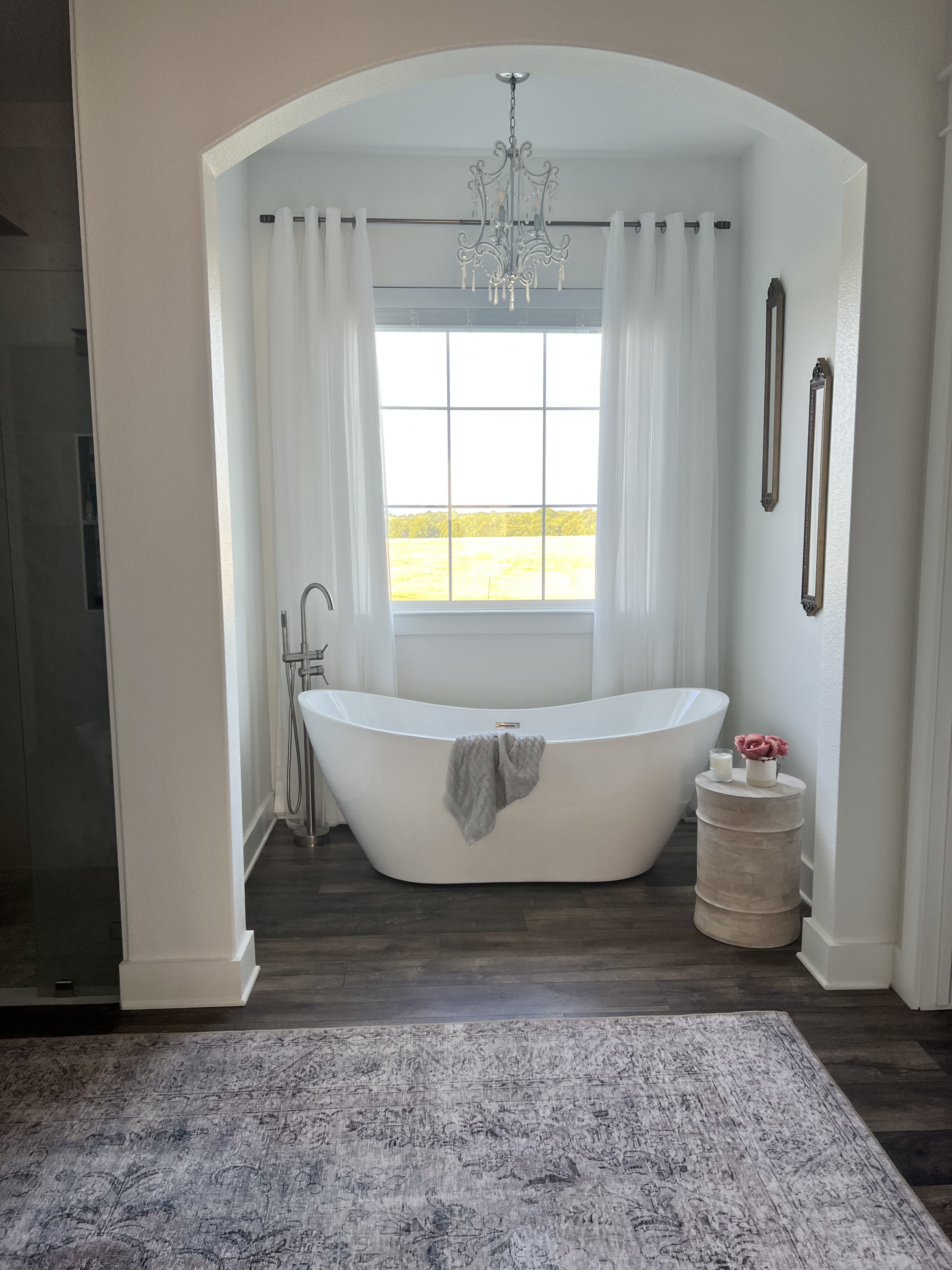 Old Gin primary bathroom — freestanding soaking tub in arched alcove with rug and chandelier