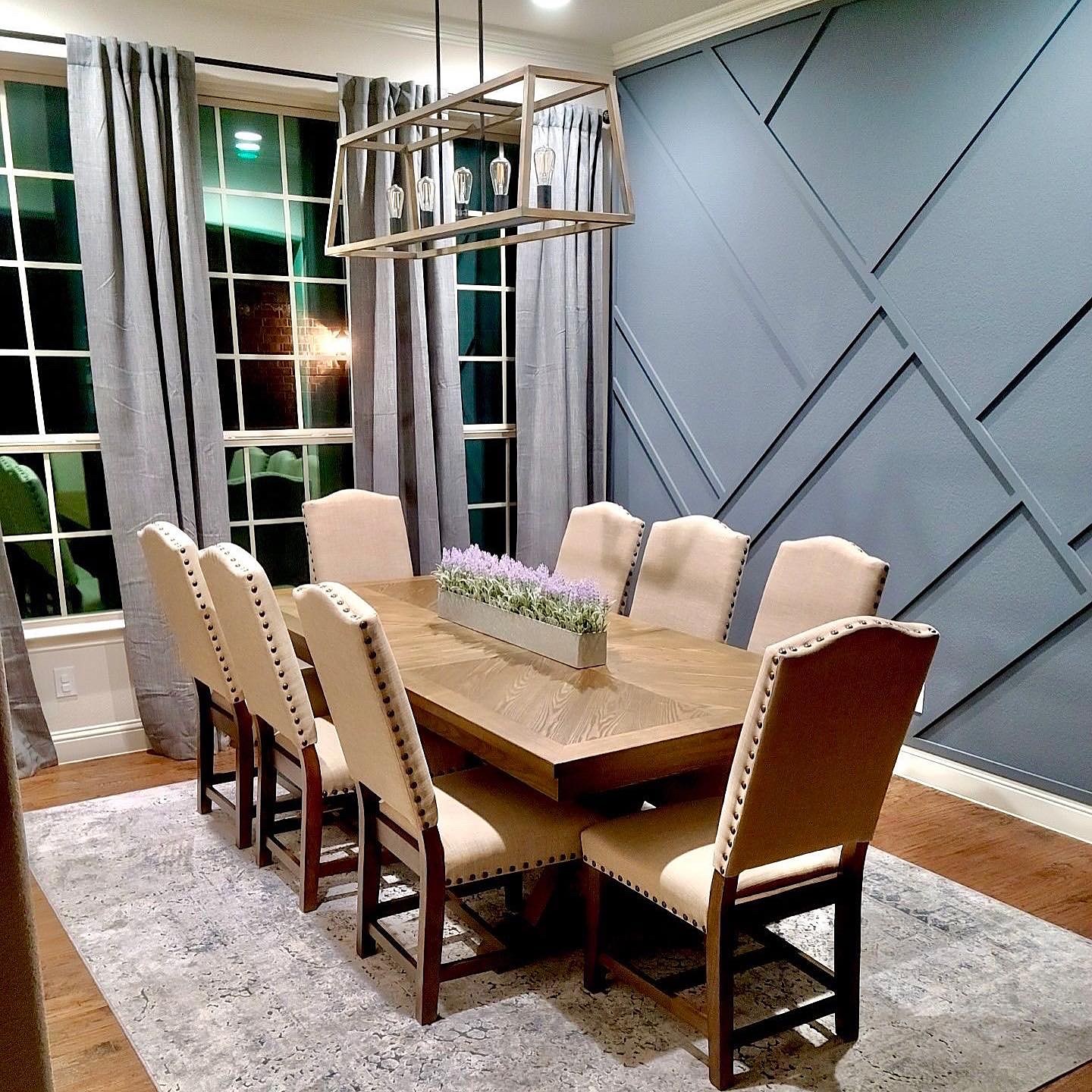 Pamela Lane dining room after — full room view with geometric slate-blue accent wall, rectangular chandelier, linen chairs with nailhead trim, herringbone table and area rug