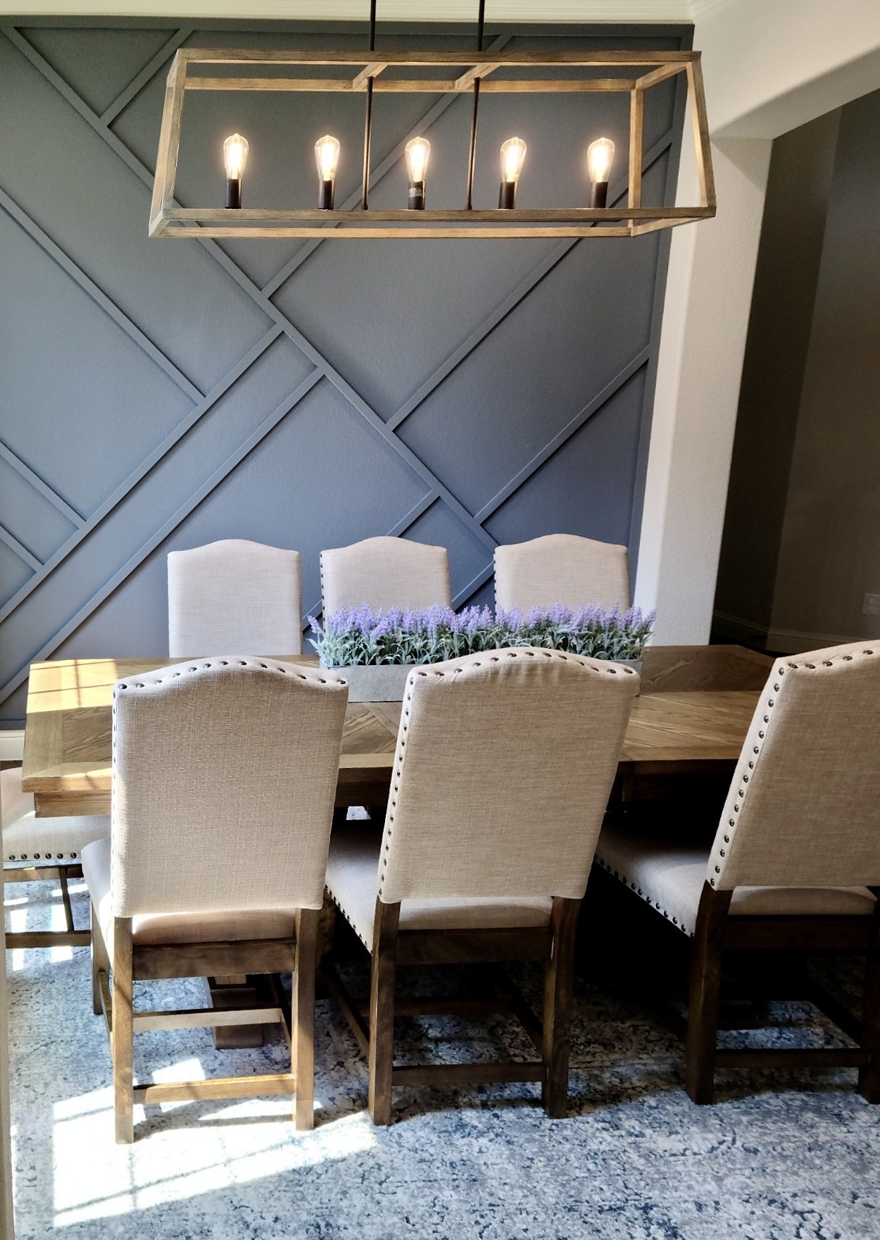 Pamela Lane dining room after — close view of the chandelier centered against the full geometric accent wall with linen chairs and lavender centerpiece below