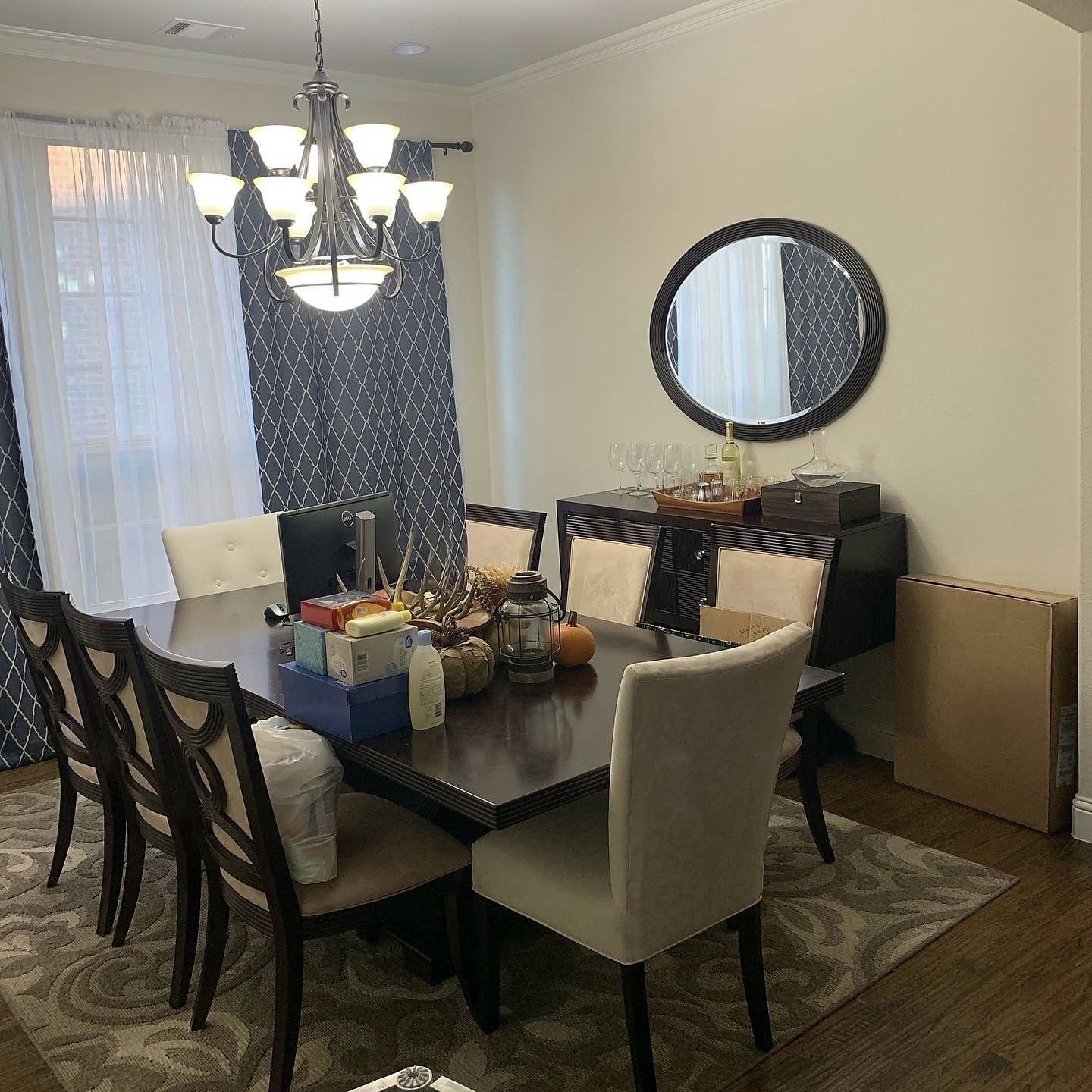 Pamela Lane dining room before — original dark wood table and mismatched chairs, traditional chandelier, patterned curtains and round mirror with sideboard
