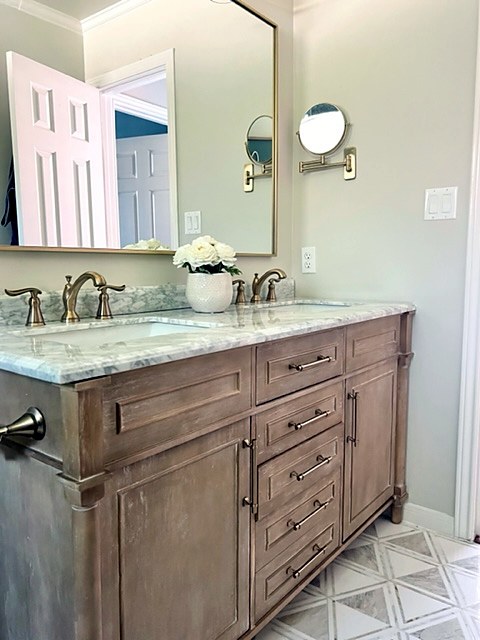 Shady Oaks — feminine bathroom double vanity with wood cabinetry, marble countertop, gold sconces and triangle floor tile