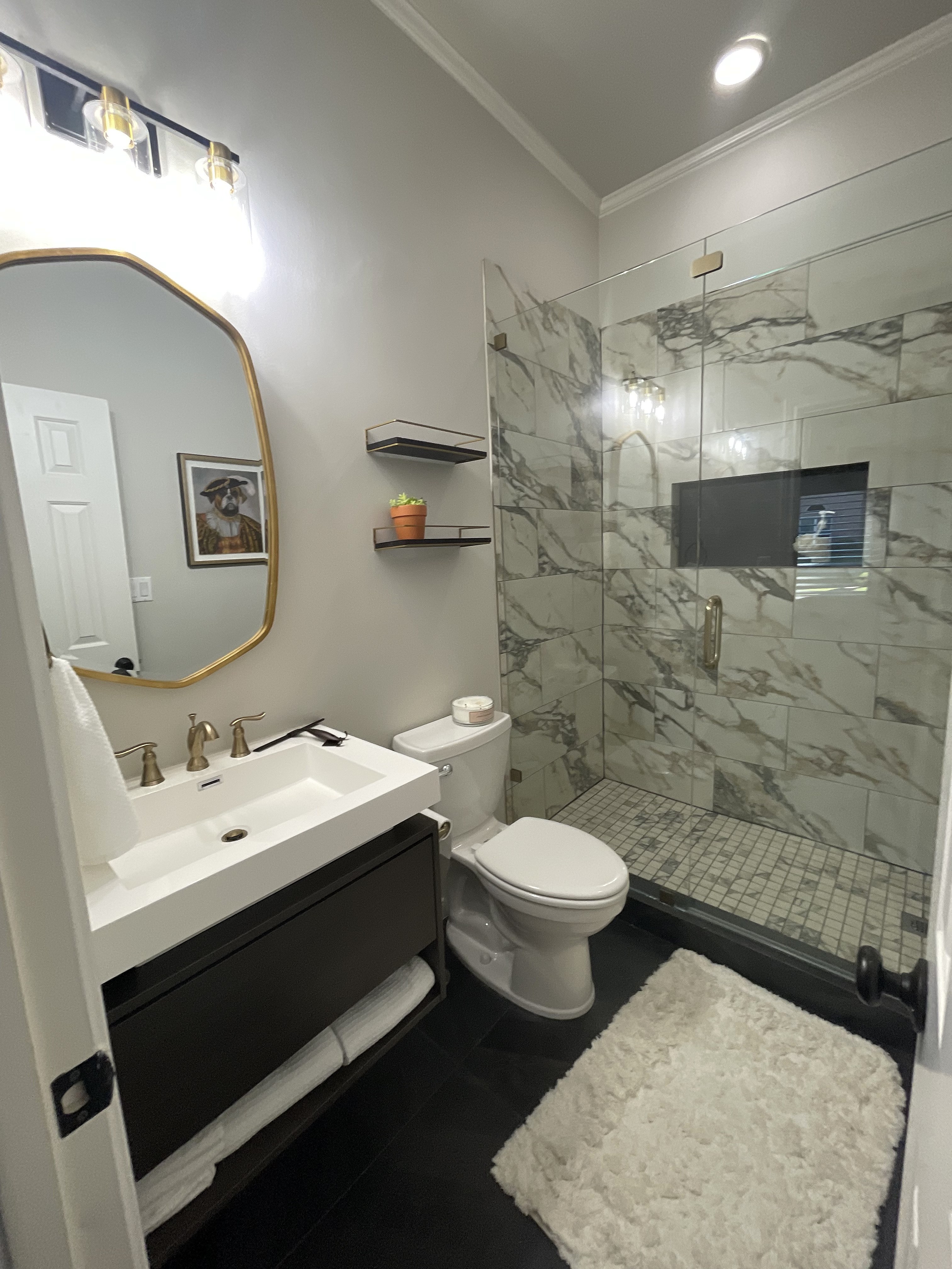 Shady Oaks — masculine bathroom with floating matte black vanity, gold mirror, marble shower and dark floor tile